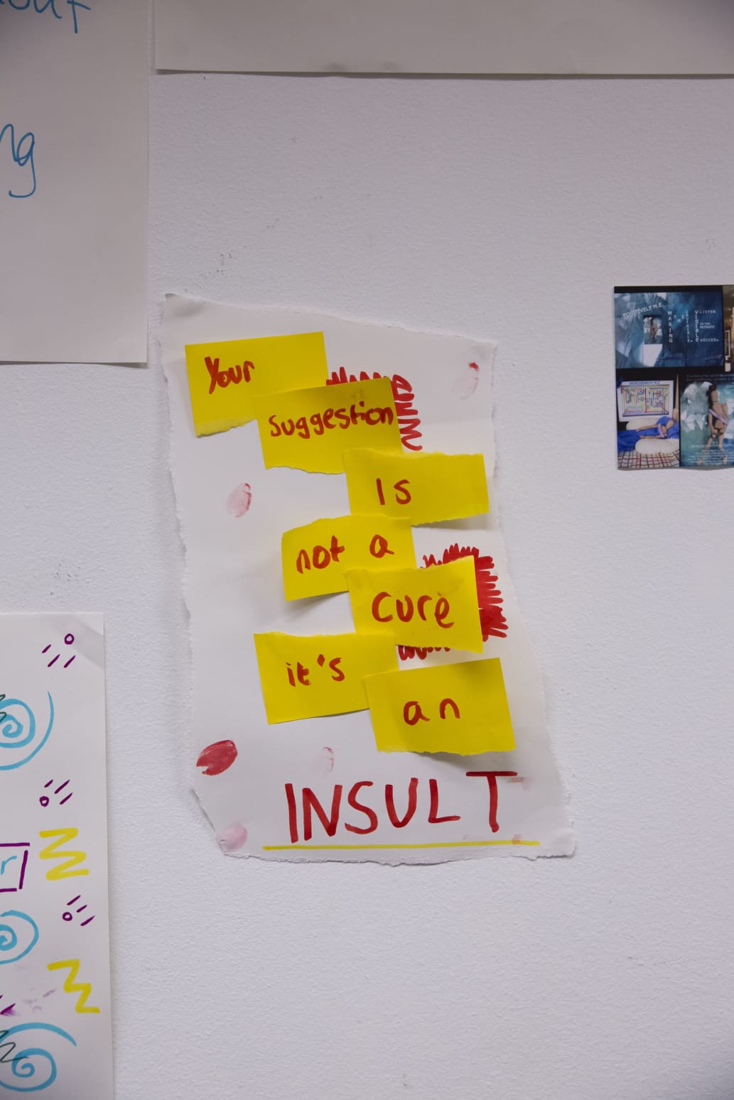 A photograph of a poster created in a workshop using paper, sticky notes, and felt tip pens. Across seven yellow post-it notes stuck to a sheet of white paper, text - written in red felt pen - reads: 