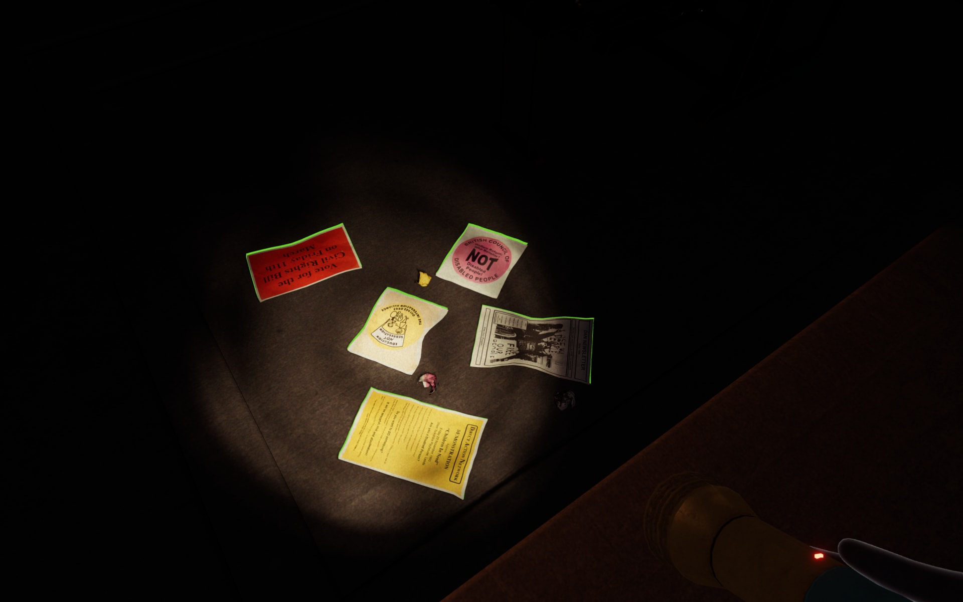 In-game screenshot focusing on a collection of paper materials strewn across the floor. The space is poorly lit, perspective limited by the reach of the torchlight. The only discernible objects are 5 pieces of paper, some slightly crumpled, laying on the floor. Only some of the text is legible - ‘Vote for the Civil Rights Bill on Friday 11th March’ and ‘Direct Action Network’.
