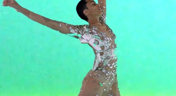 Image of a performer, arms extended and wearing a shiny bodysuit, before a bright green background. Image is overlaid with BSL and captioning symbols. Image courtesy of Alexandrina Hemsley, from Maelstrom Under Glass Alexandrina Hemsley, Yewande 103 (2020).