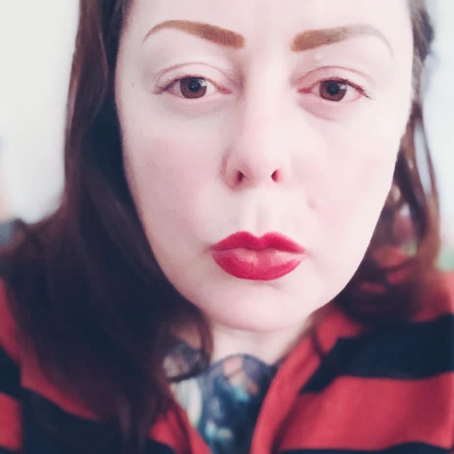 A selfie of a woman with brown hair wearing red lipstick.