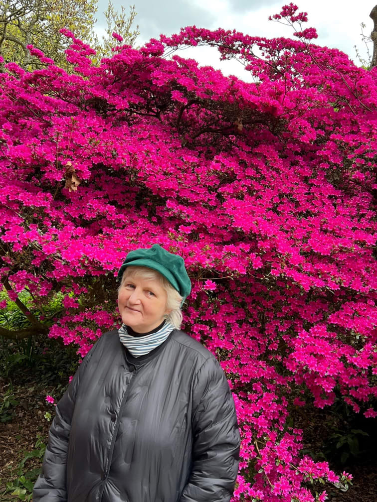 Photograph of Mandi, a middle-aged white woman with short blonde hair, stood in front of a blossoming tree.