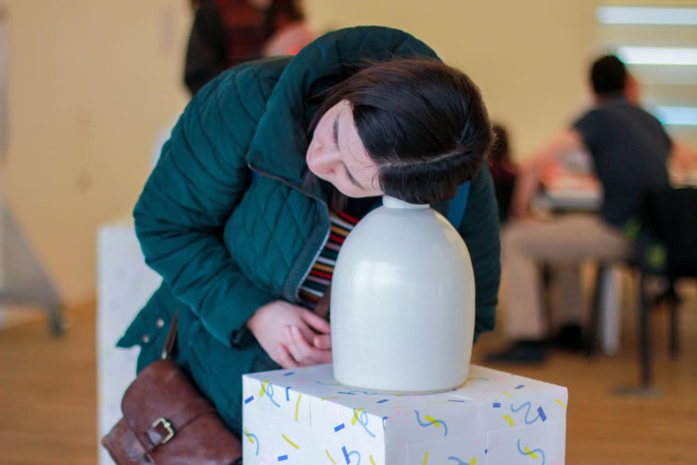A women leans down to listen to the top of an audio vase on a plinth at Tate Exchange