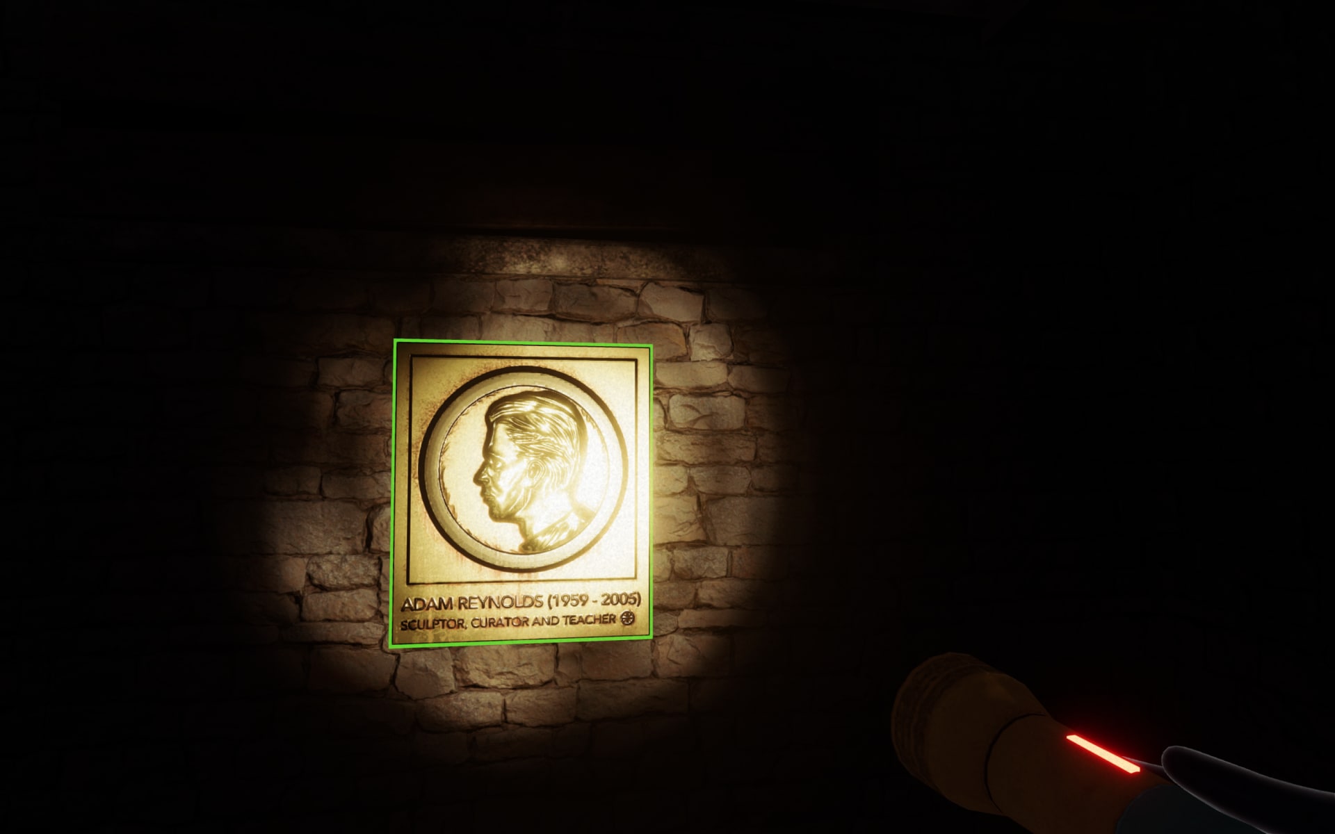 In-game screenshot depicting a plaque mounted on a dark brick wall. Perspective is limited by the reach of the torchlight. In front of the user, on the wall, a golden metal plaque is highlighted by both the torch and a thin neon green outline, indicating it is an interactive object. On the plaque, within a circle, is the side profile of a man. Beneath is text reading ‘Adam Reynolds. Sculptor, Creator, and Teacher.’