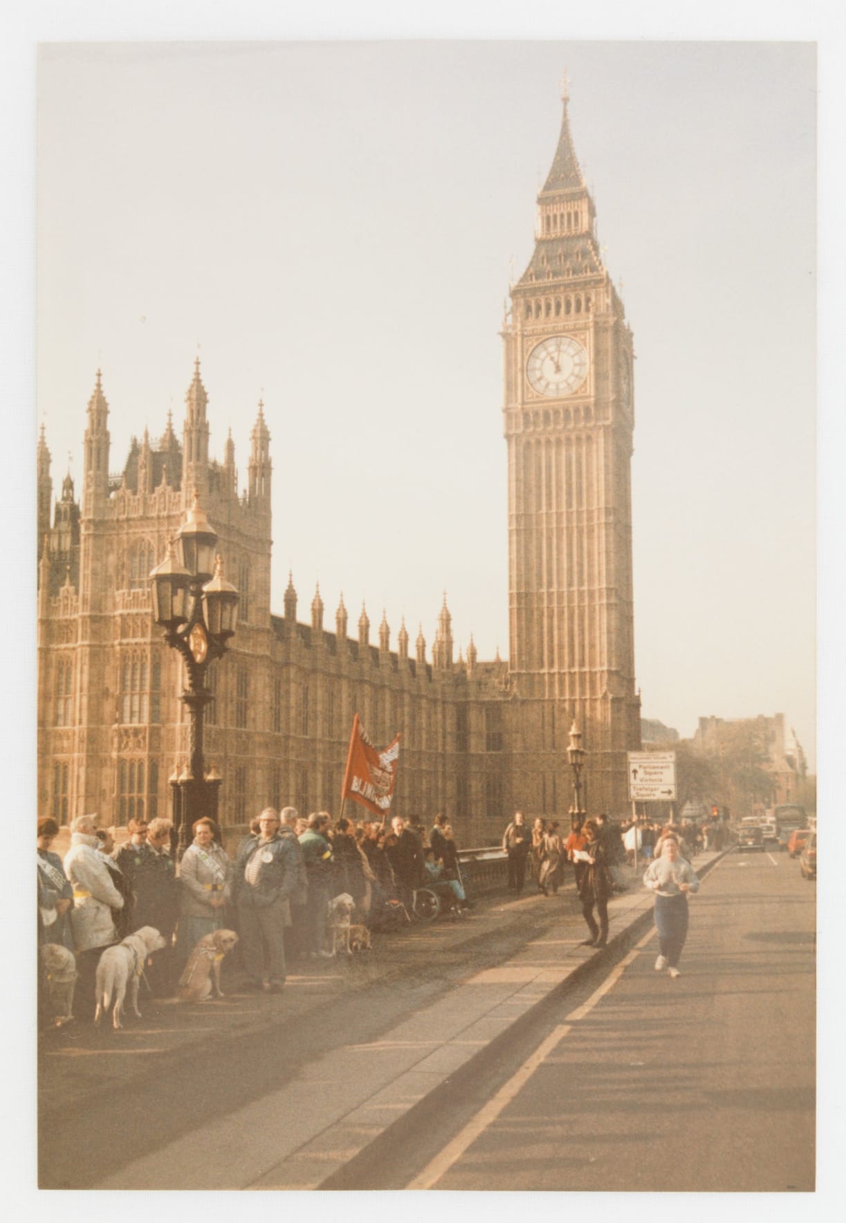 An old photograph taken on a London bridge, in view of Big Ben and the Houses of Parliament. Protestors line the street holding signs.