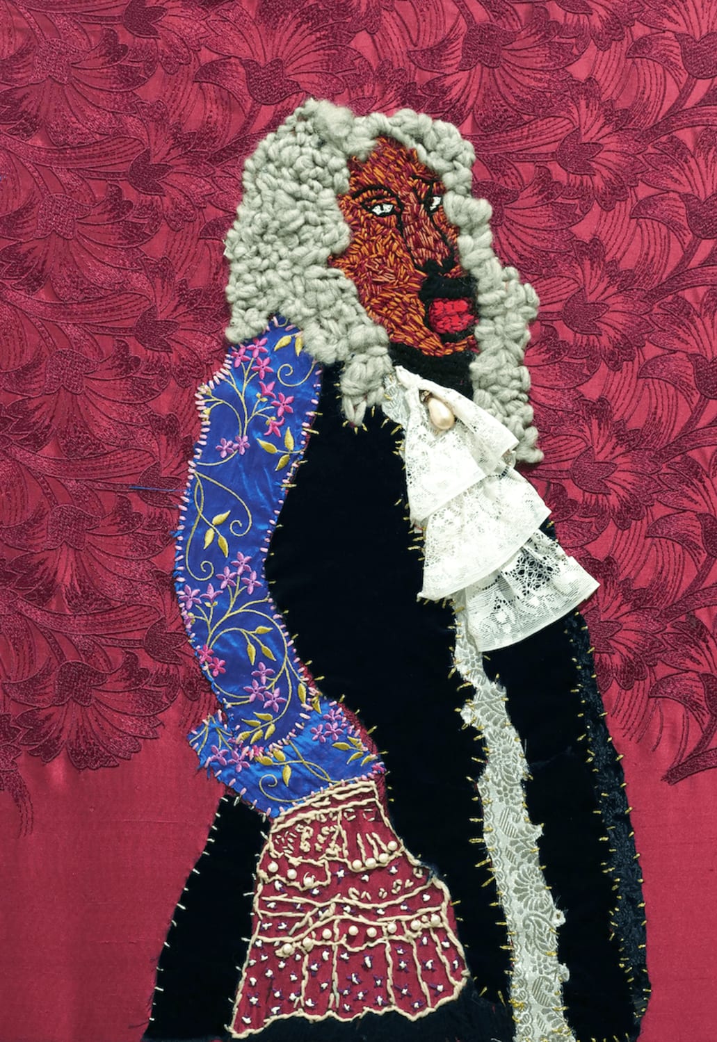 An embroidered and appliqued image of a black man in white powdered wig, which reaches just past the shoulders. He holds a stately posture, standing in front of a red floral background. Patches of fabric have been roughly sewn to illustrate his 17th century costume.  White stab stitching has been worked at the end of his jacket to suggest a long drooping lace sleeve.. 