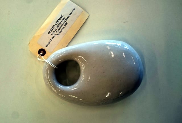 smooth ceramic object with grey hues, the shape of an oval bar of soap, with a hole near to the narrow end; the object has a small exhibition tag with artist details in small print