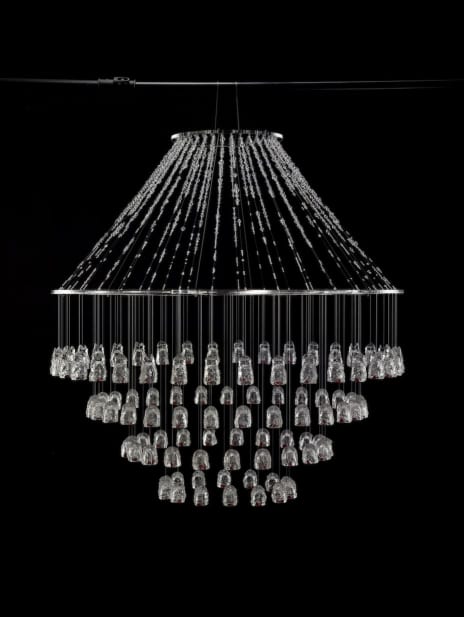 On a black background hangs a chandelier made out of tiny resin objects and string. The low light picks up the string and the hanging pieces.
