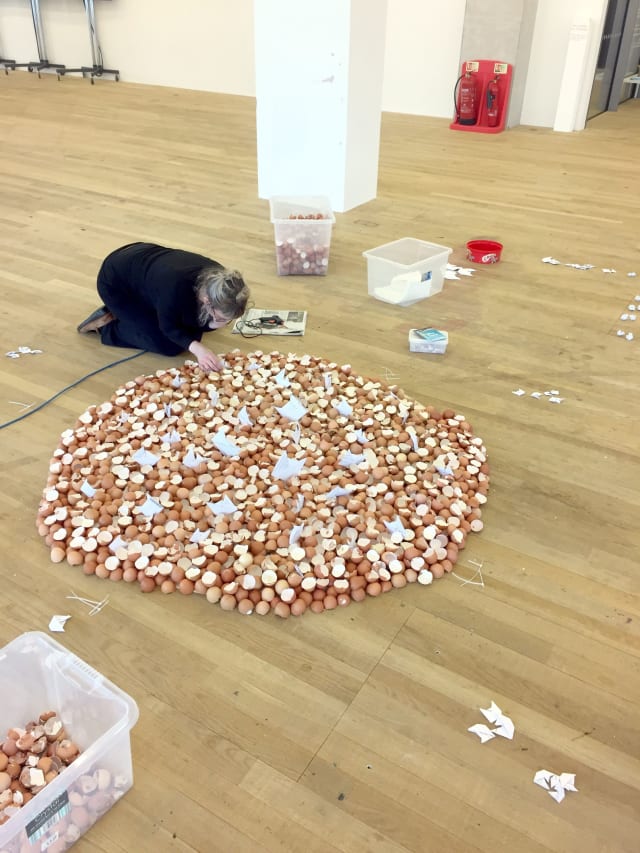 Artist Anna Berry adding broken eggshells to the existing shells lying in a circle on the floor at Tate Exchange