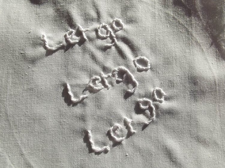 Close up of a white linen coth with the words let go let go let go embroidered on it