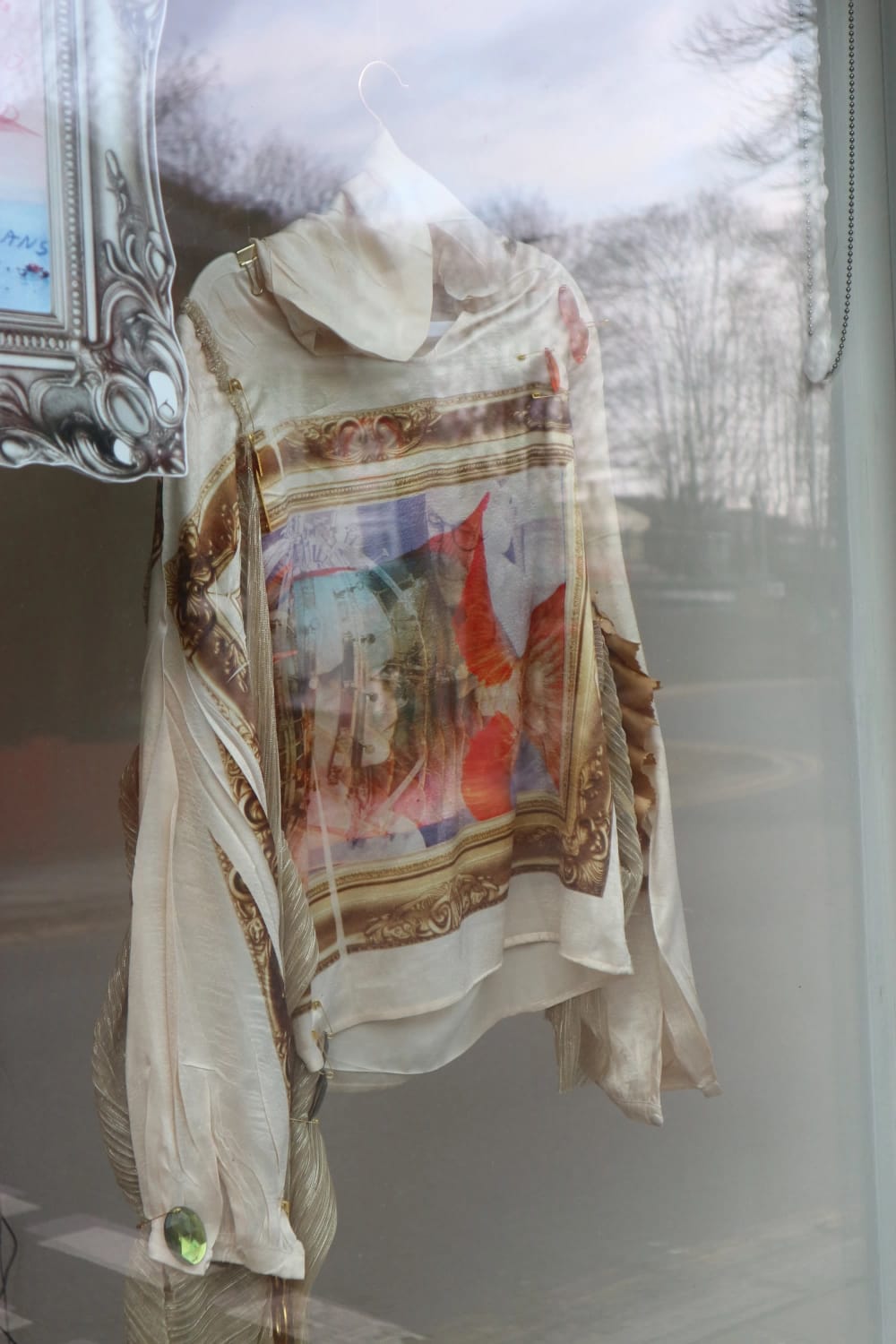 A decorated floaty garment hangs in a large window.