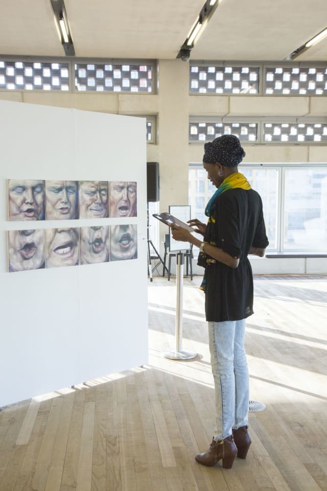tall woman viewing small square paintings hung on white standing walls at tate exchange, artworks are of from the Shortlist 2017